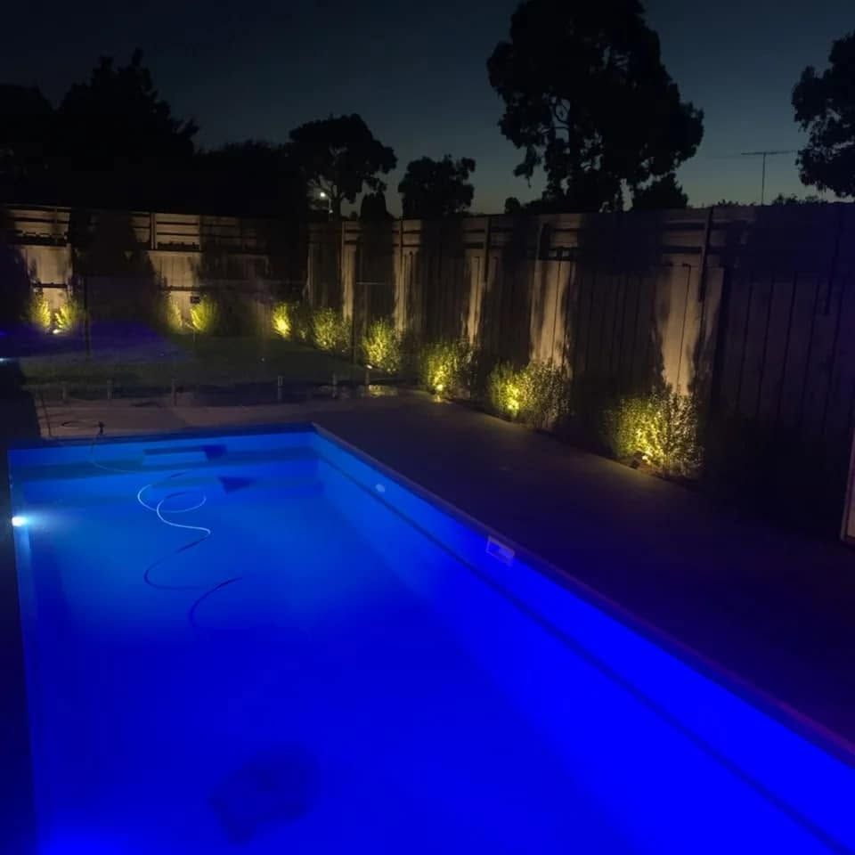 Pool lit blue at night with uplights along the garden bed